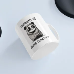 Uroczy kubek z pandą na białym tle przedstawiający pandę zawiniętą w kołderkę i napisem "Schowamy się przed światem?"