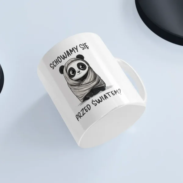 Uroczy kubek z pandą na białym tle przedstawiający pandę zawiniętą w kołderkę i napisem "Schowamy się przed światem?"